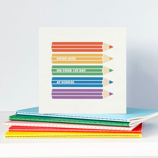 Stack of colourful notebooks with a card featuring rainbow coloured pencils on a white surface.