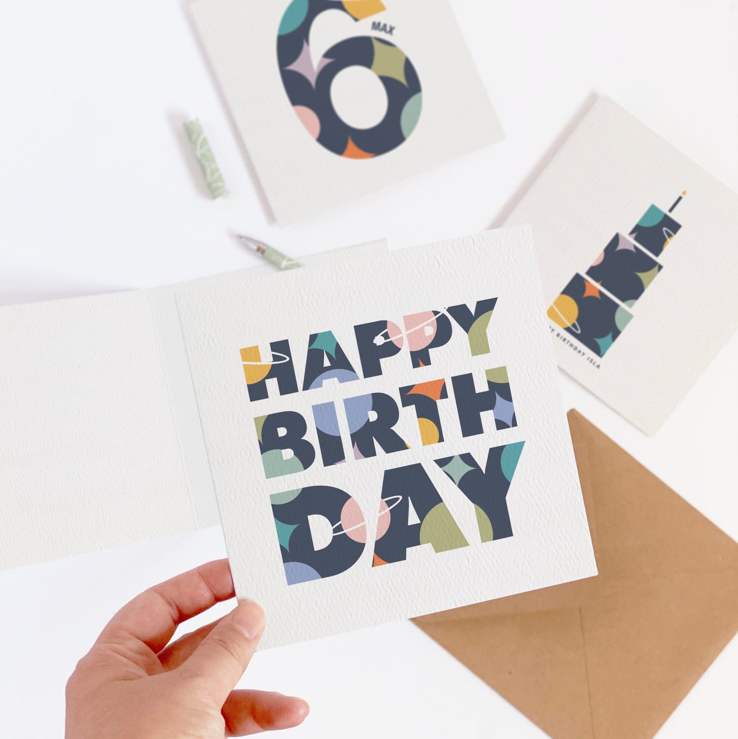 Colorful 'Happy Birthday' card held by a hand with other birthday cards on a white background
