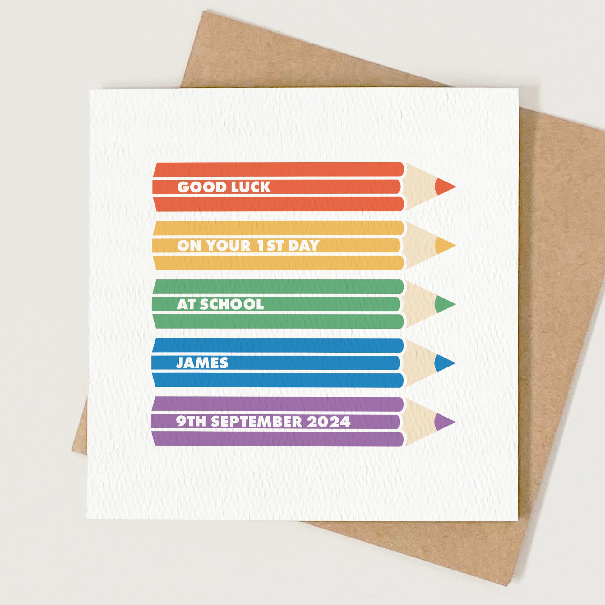 White greeting card with 5 rainbow coloured pencil crayons illustrations on, each with text on that reads 'good luck on your first day at school James, 9th September 2024'