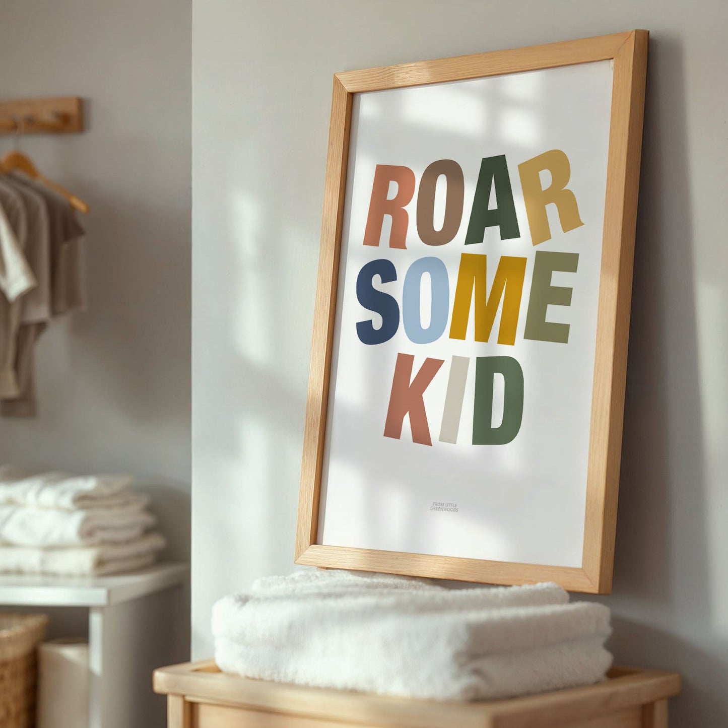 Framed poster with 'ROAR SOME KID' text in a room with folded clothes and a basket.