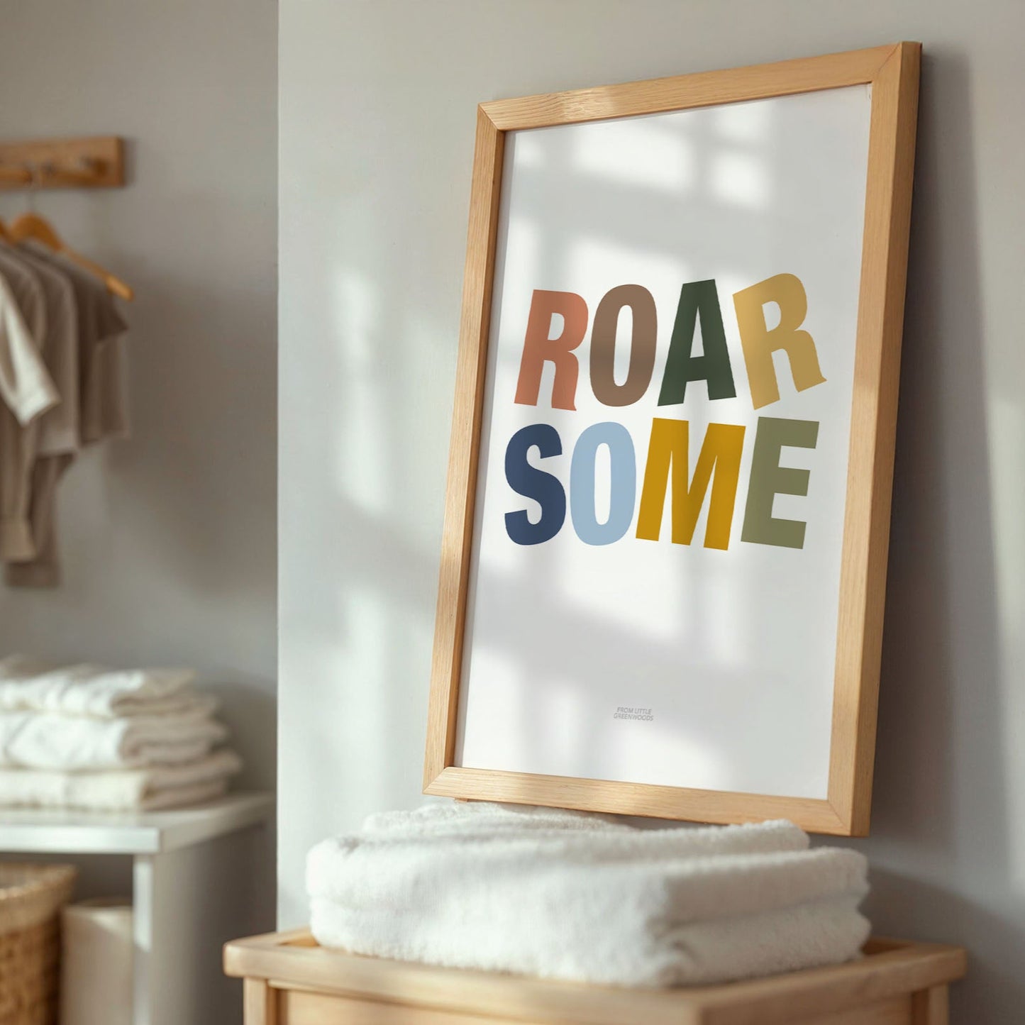 Framed poster with 'ROAR SOME' text in a home setting with towels and baby clothing.