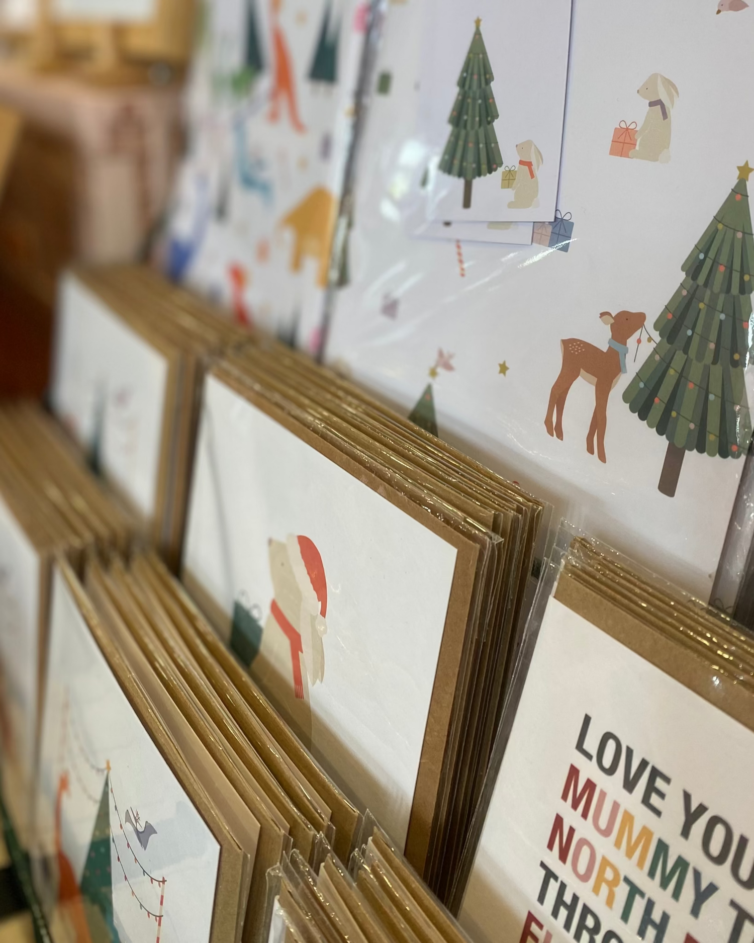 Display of Christmas greeting cards and wrapping paper with various designs on a rack.