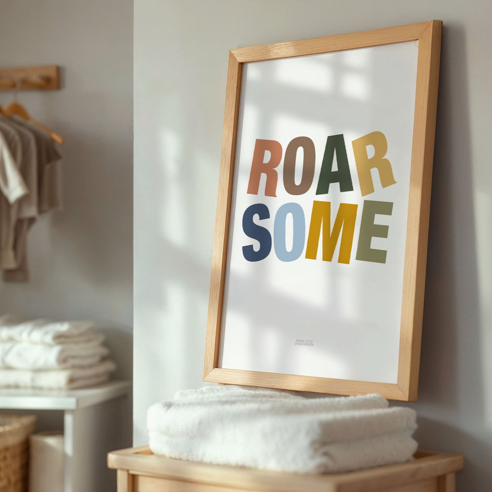 Framed poster with 'ROAR SOME' text in a home setting with towels and baby clothing.