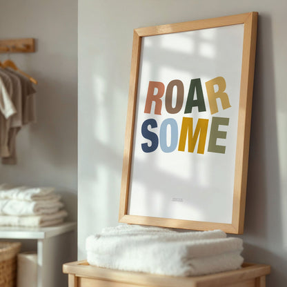 Framed poster with 'ROAR SOME' text in a home setting with towels and baby clothing.