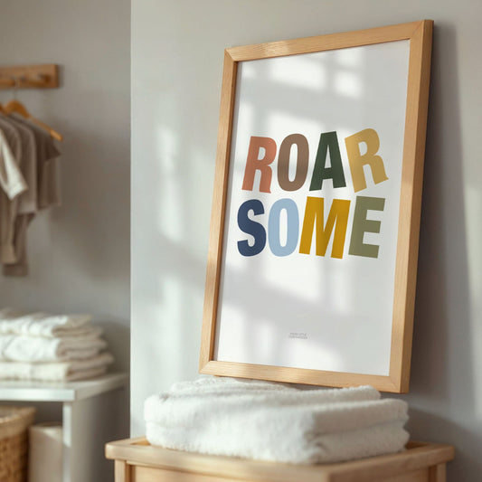 Framed poster with 'ROAR SOME' text in a home setting with towels and baby clothing.